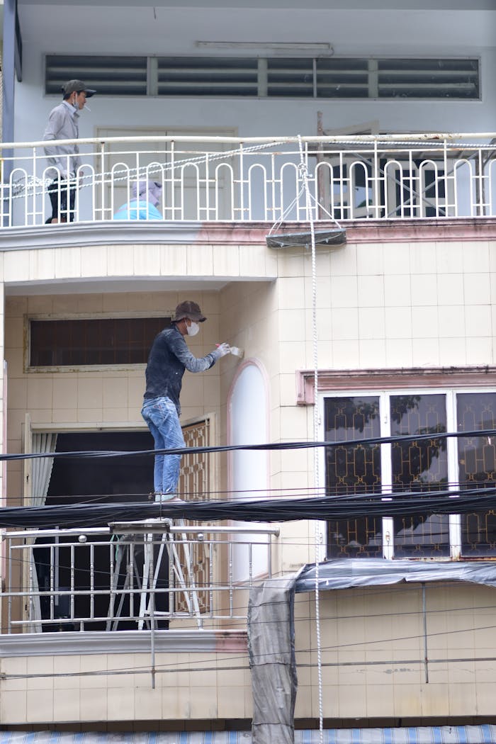 Two workers painting a building facade from a scaffold on an urban street.